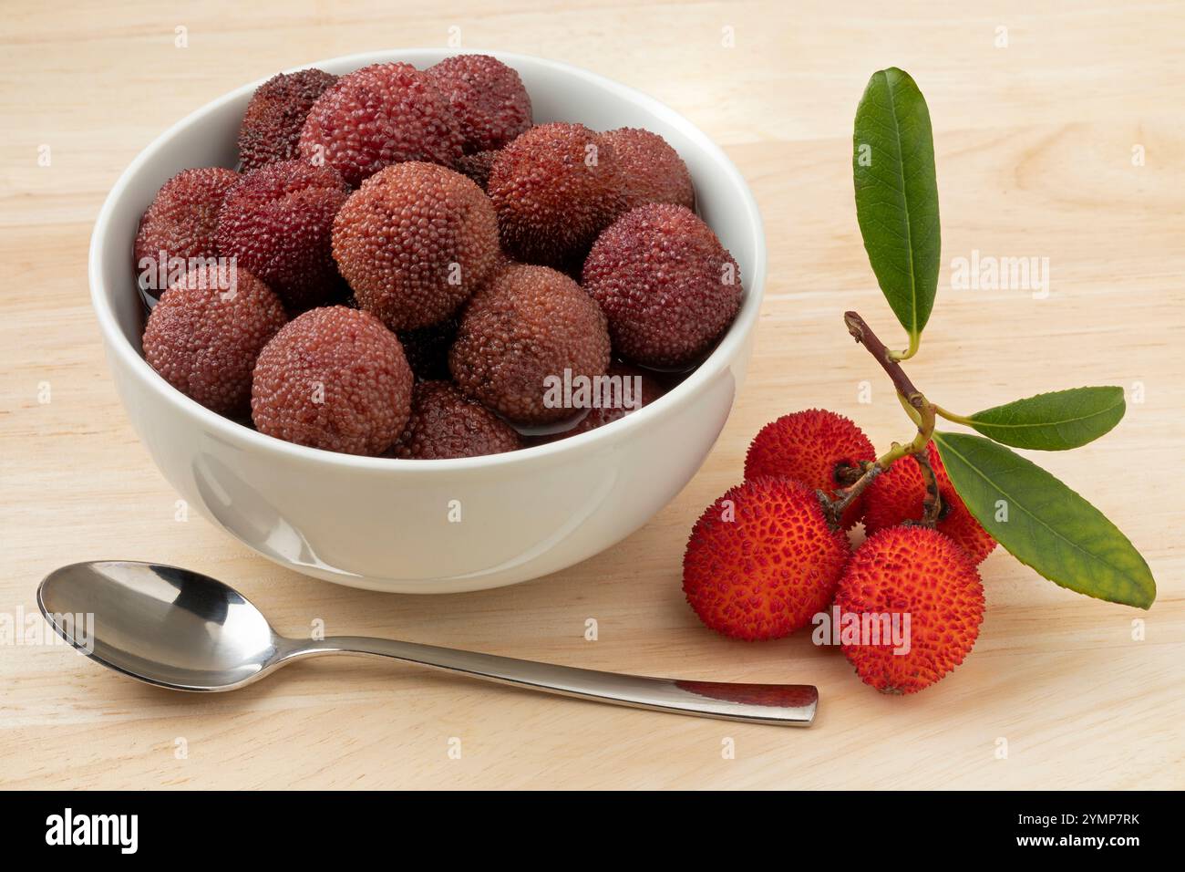 Ciotola in ceramica con bacche di Arbutus in sciroppo da vicino e quelle fresche mature davanti Foto Stock