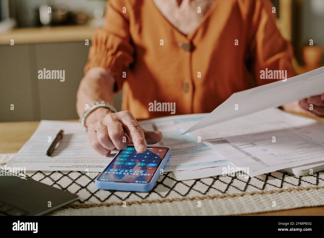 Donna anziana che lavora con documenti e smartphone, gestisce i registri finanziari a casa. Senior che si concentra sulla gestione di bollette e rendiconti finanziari sul tavolo Foto Stock