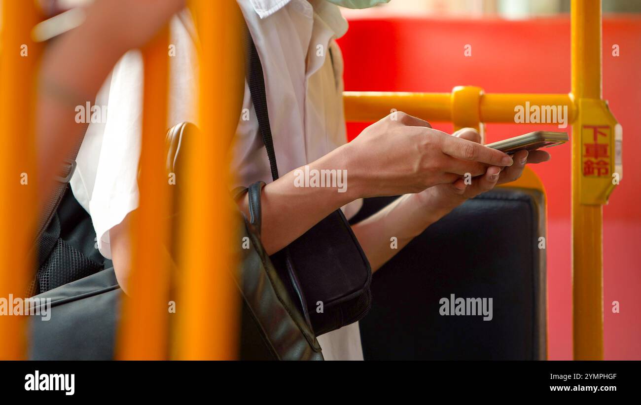 Un giovane pendolare che indossa una maschera utilizza uno smartphone su un autobus. Le barre di appoggio gialle contrastano con la camicia bianca dell'uomo, catturando un momento di modernità Foto Stock