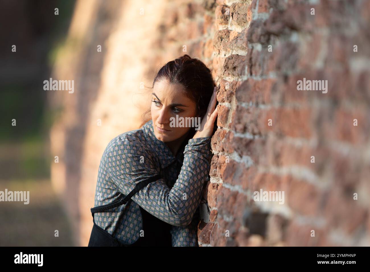 Una donna triste con la mano su un antico muro di mattoni sta riflettendo sulla vita Foto Stock