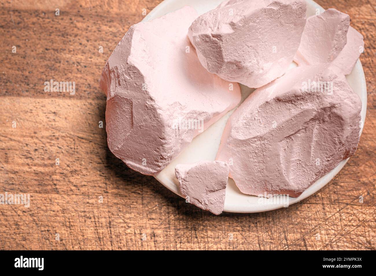 Pezzi di argilla rosa commestibile o gesso su sfondo di legno, vista dall'alto, spazio per copiare. Argilla di calcio naturale per il cibo. Foto Stock