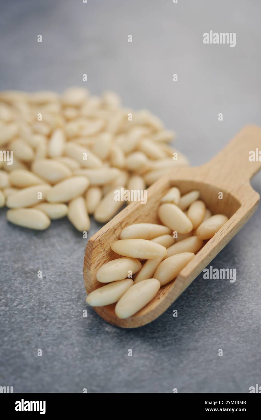 Cucchiaio in legno ripieno di noci di pino crudi freschi su sfondo grigio Foto Stock