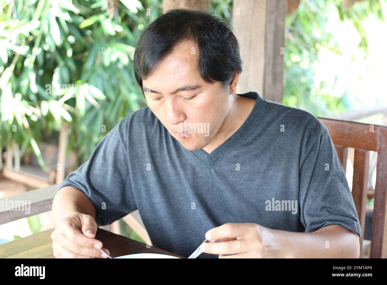 Un uomo gode di un pasto in un ambiente tranquillo all'aperto, circondato dal verde. Si concentra sull'assaporare il suo cibo, riflettendo un momento di piacere culinario. Foto Stock