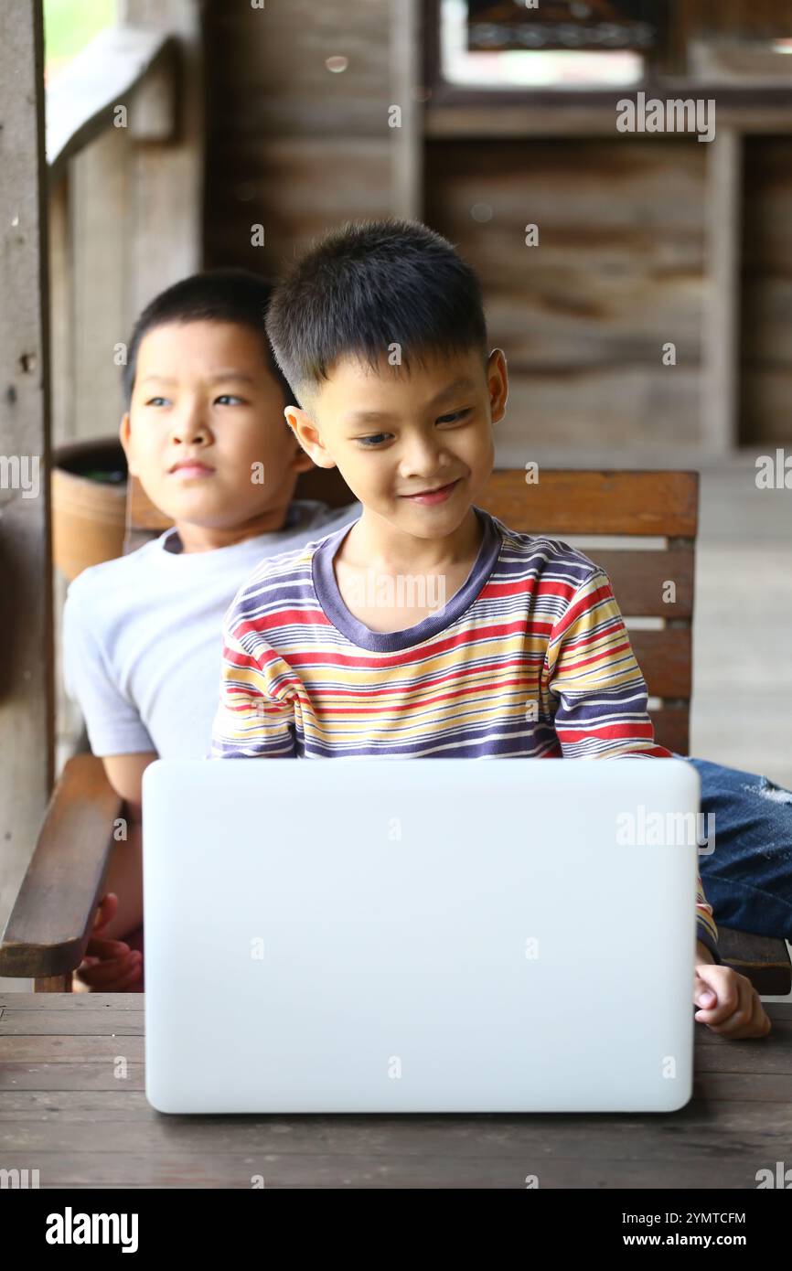 Due ragazzi condividono un momento su un notebook in un ambiente rustico, mostrando amicizia, curiosità e gioia di imparare attraverso la tecnologia. Foto Stock