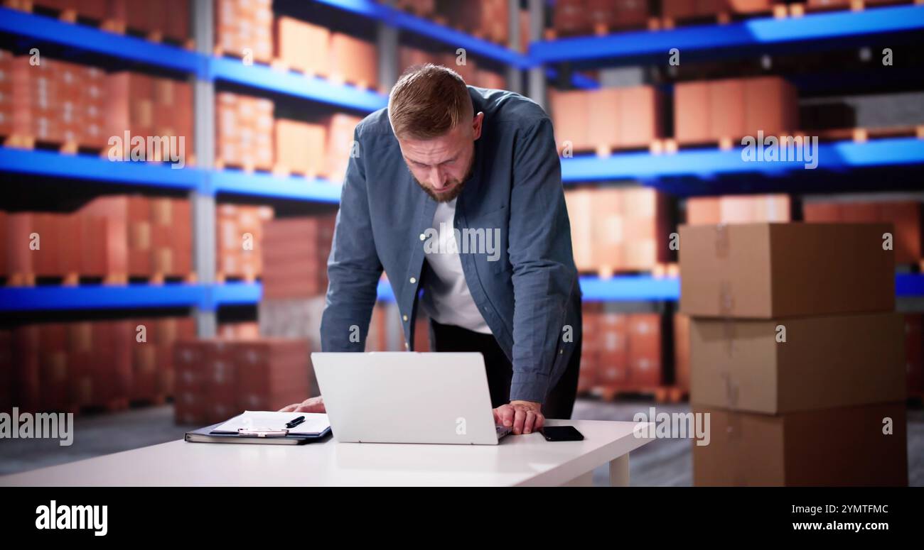 Uomo d'affari che utilizza un computer portatile in magazzino per la gestione dell'inventario Foto Stock