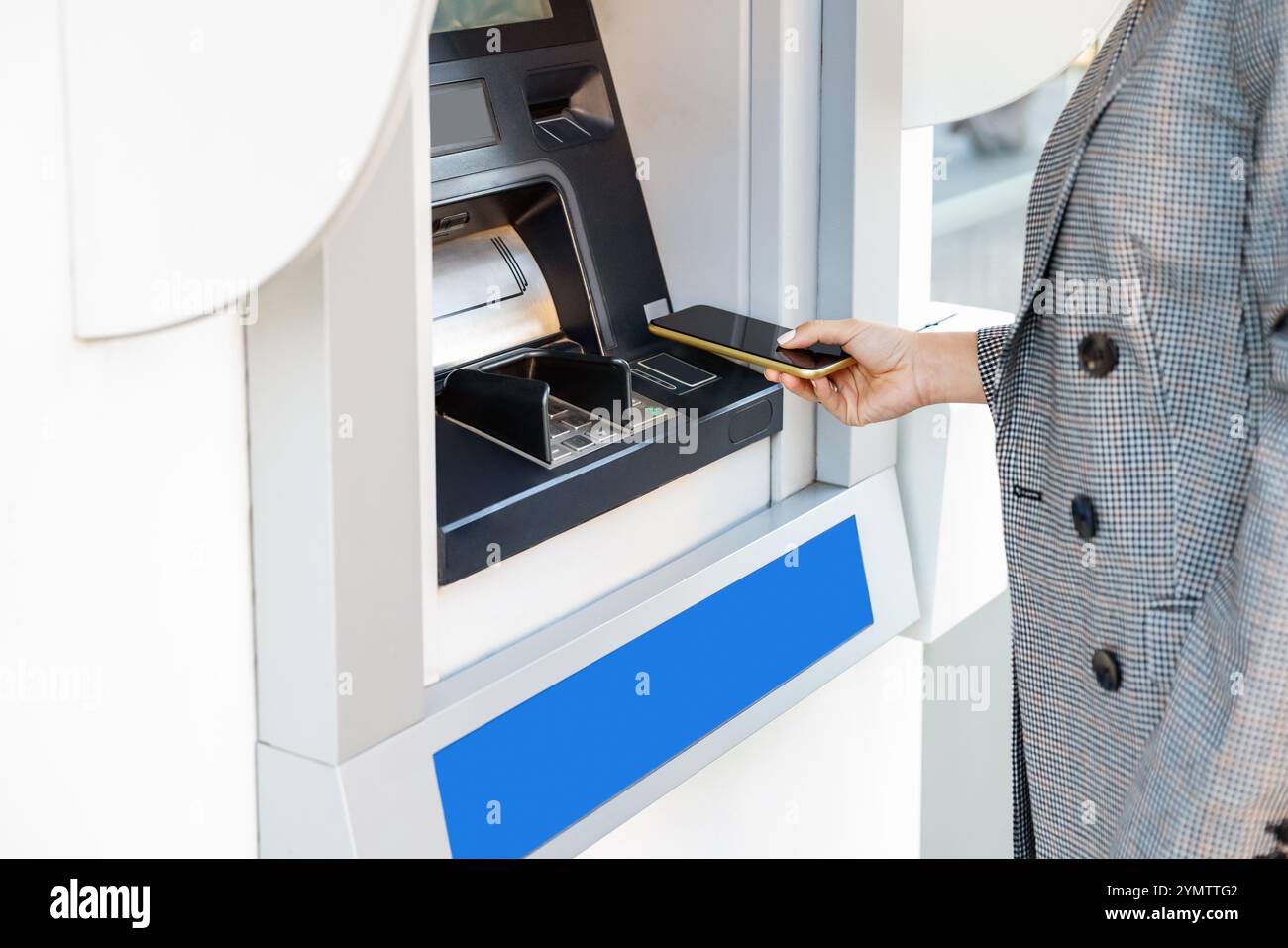 Persona che utilizza lo smartphone per il prelievo di contante allo sportello Bancomat. Foto Stock