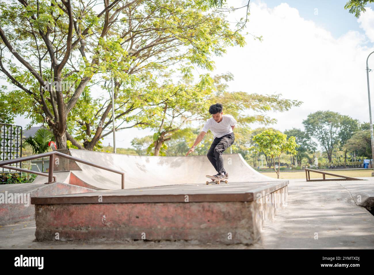 Un giovane skateboarder esegue un trucco in un vivace skate Park sotto il cielo limpido. Foto Stock