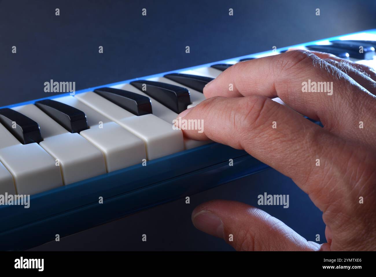 Dettaglio della melodica blu suonata dalla mano con sfondo blu e fascio luminoso illuminante. Foto Stock