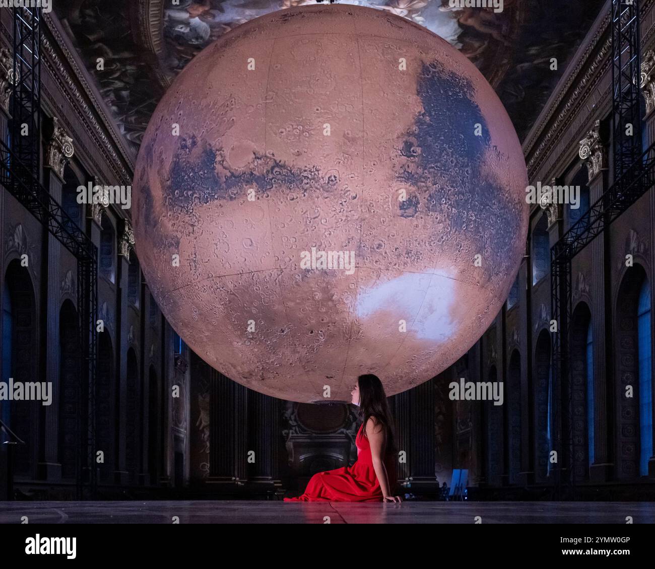 Londra, Regno Unito. 23 novembre 2024. Un membro dello staff con ‘Mars’ dell’artista Luke Jerram che è in mostra presso l’Old Royal Naval College di Greenwich, fino al 20 gennaio 2025. Con un diametro di 7 m, l'opera d'arte a rotazione lenta presenta immagini dettagliate della superficie marziana ricreate in scala e sovrapposte allo sfondo della Painted Hall di Sir James Thornhill, che presenta oltre 3.700 metri quadrati di pareti e soffitti barocchi. Crediti: Stephen Chung / Alamy Live News Foto Stock