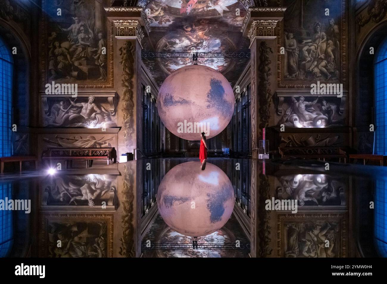 Londra, Regno Unito. 23 novembre 2024. Un membro dello staff con ‘Mars’ dell’artista Luke Jerram che è in mostra presso l’Old Royal Naval College di Greenwich, fino al 20 gennaio 2025. Con un diametro di 7 m, l'opera d'arte a rotazione lenta presenta immagini dettagliate della superficie marziana ricreate in scala e sovrapposte allo sfondo della Painted Hall di Sir James Thornhill, che presenta oltre 3.700 metri quadrati di pareti e soffitti barocchi. Crediti: Stephen Chung / Alamy Live News Foto Stock