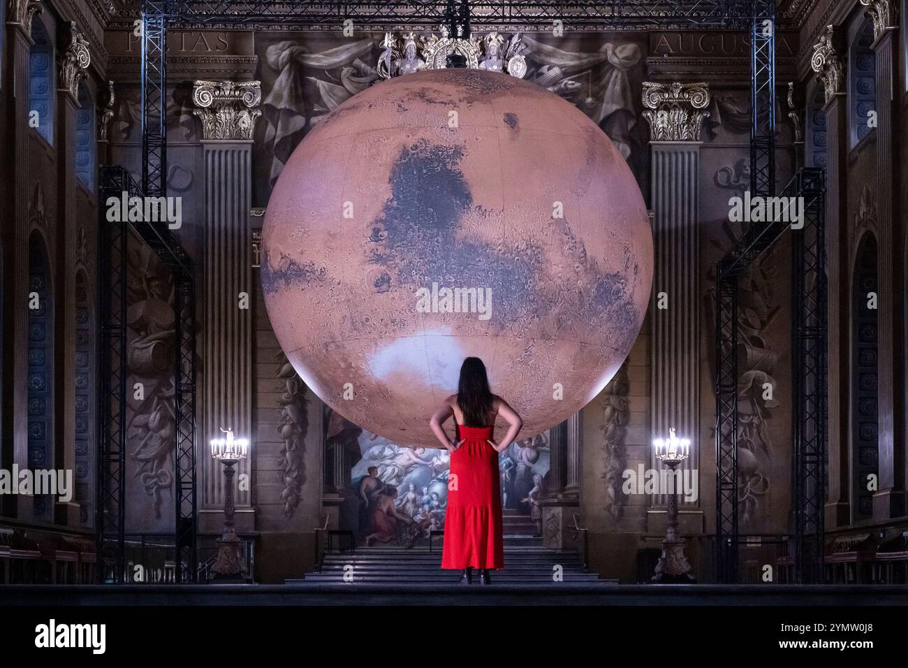 Londra, Regno Unito. 23 novembre 2024. Un membro dello staff con ‘Mars’ dell’artista Luke Jerram che è in mostra presso l’Old Royal Naval College di Greenwich, fino al 20 gennaio 2025. Con un diametro di 7 m, l'opera d'arte a rotazione lenta presenta immagini dettagliate della superficie marziana ricreate in scala e sovrapposte allo sfondo della Painted Hall di Sir James Thornhill, che presenta oltre 3.700 metri quadrati di pareti e soffitti barocchi. Crediti: Stephen Chung / Alamy Live News Foto Stock