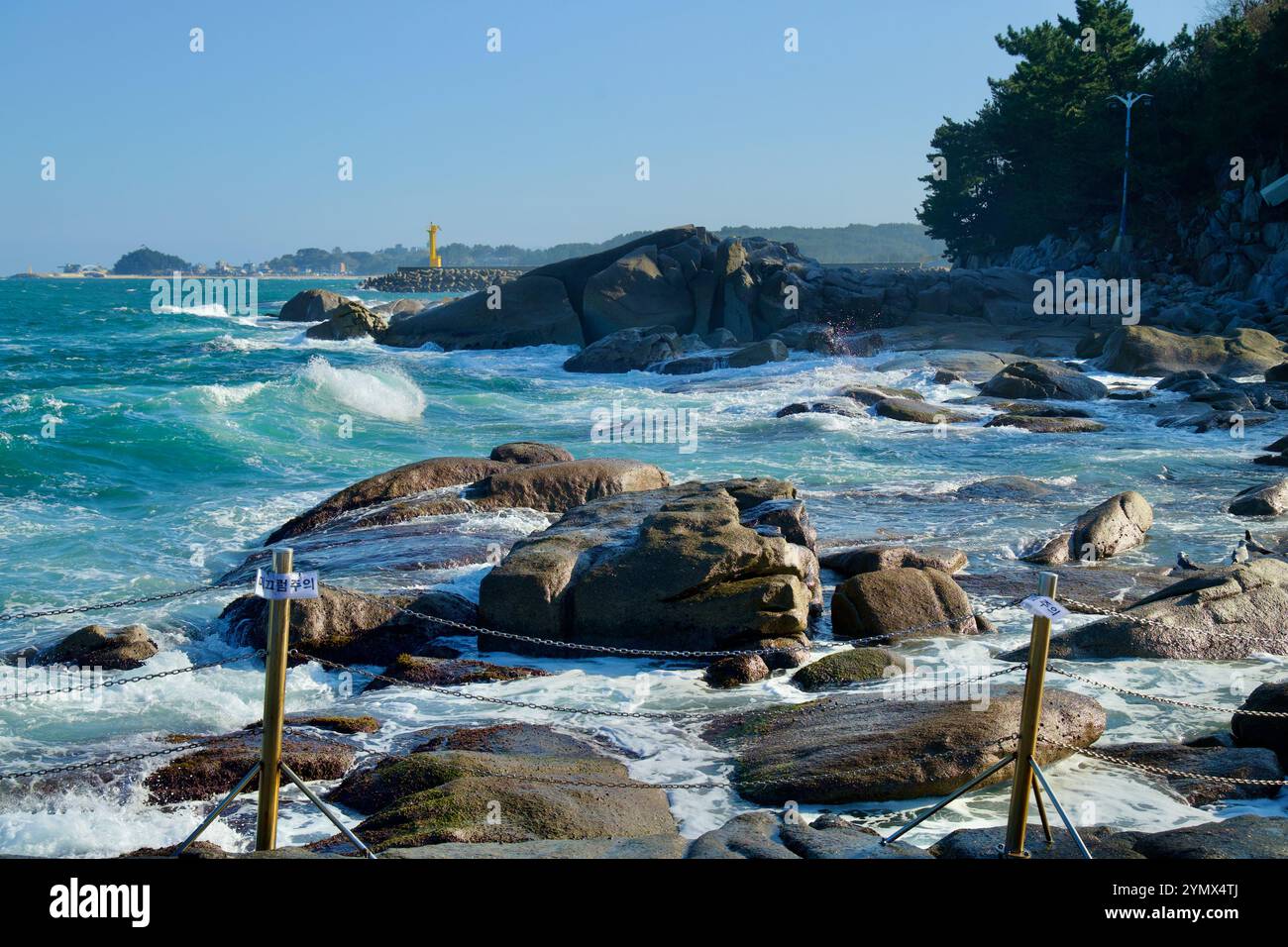 Contea di Yangyang, Corea del Sud - 3 novembre 2024: Rocce aspre vicino a Yeonhwadae incontrano le dinamiche onde del Mare Orientale, con un faro giallo e un faro Foto Stock