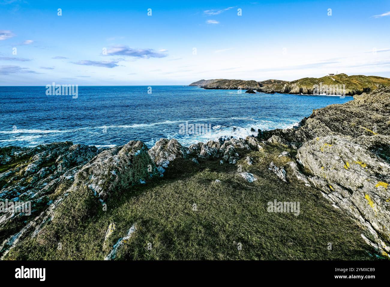 Il sole tramonta all'orizzonte, illuminando le aspre scogliere accanto al mare tranquillo. Le onde si infrangono dolcemente contro le rocce, creando una costa tranquilla Foto Stock