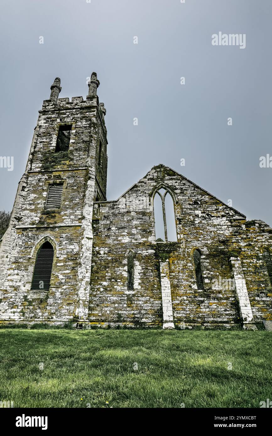 I resti di una chiesa in pietra risaltano nella tranquilla campagna, con la sua architettura storica adagiata tra erba lussureggiante in una giornata nuvolosa. Foto Stock