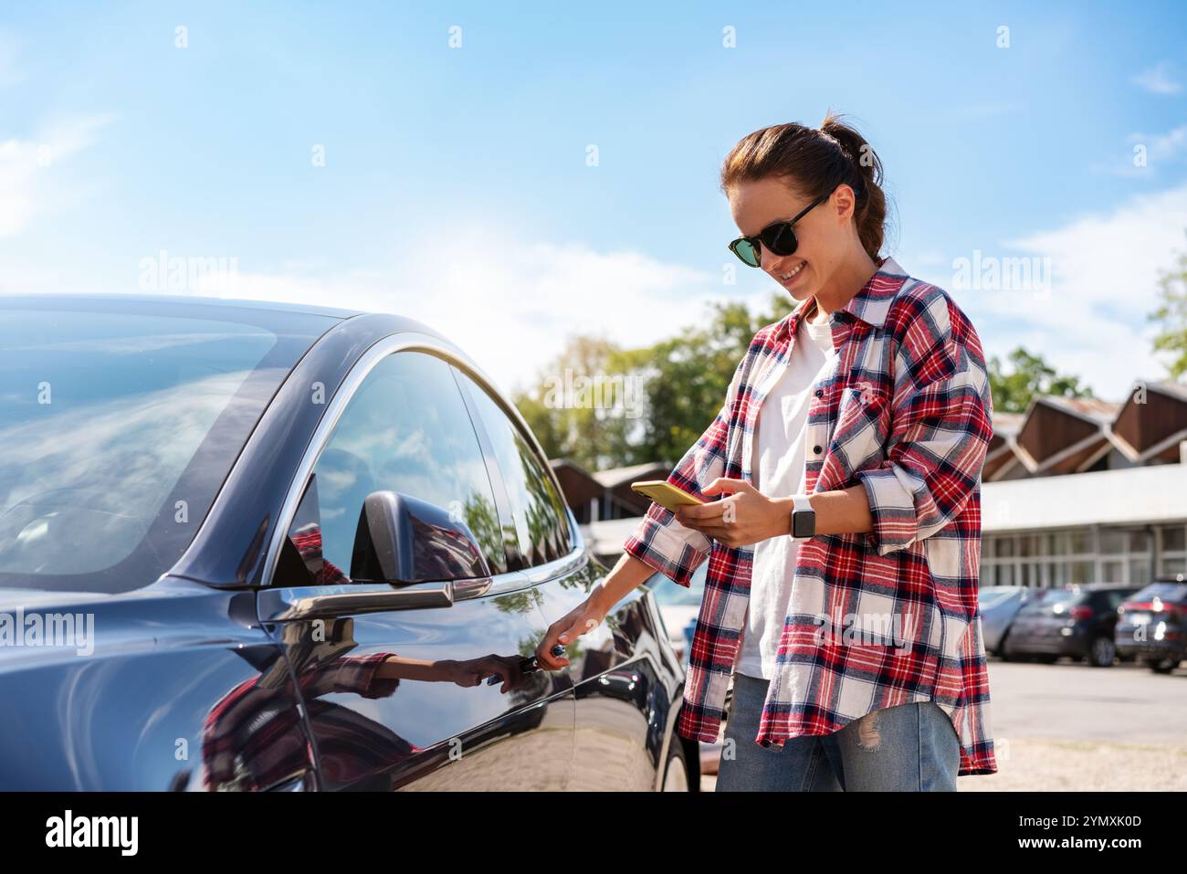 Donna caucasica in abito casual che sblocca l'auto a noleggio utilizzando il suo smartphone e l'app mobile all'aperto in estate. Foto Stock