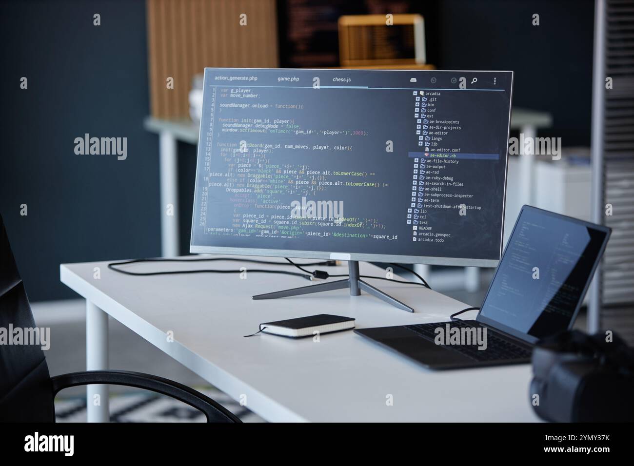 Ufficio moderno con un'interfaccia di codifica visualizzata su un monitor, accompagnata da un computer portatile e uno smartphone, che mostra vari strumenti tecnologici e gadget in W Foto Stock