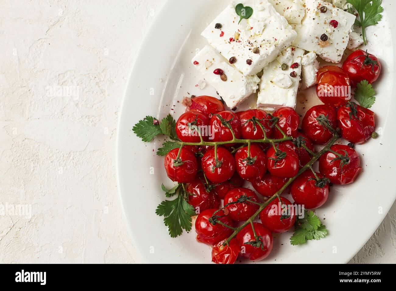 Pomodori ciliegini al forno, con formaggio e spezie, su un piatto bianco, fatti in casa, nessuno Foto Stock