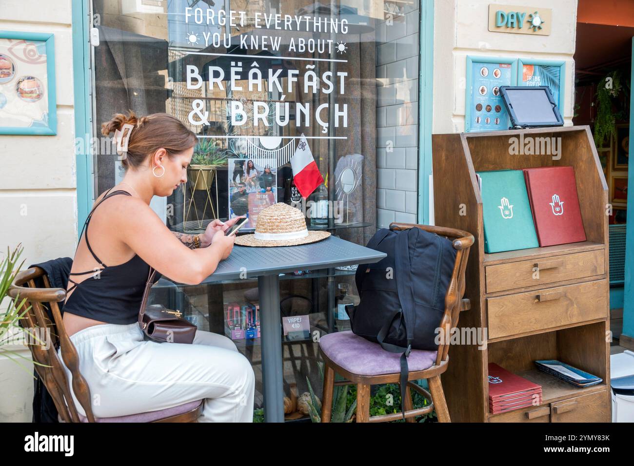La Valletta Malta, South Street, Tribe Malta Restaurant Cafe' al fresco, donna single femminile, seduta da sola, lettura a controllo, smartphone Foto Stock