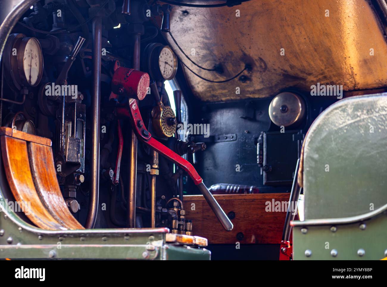 Primo piano del pannello di controllo in una locomotiva a vapore d'epoca con leve, indicatori e maniglia verniciata di rosso in un ambiente industriale Foto Stock