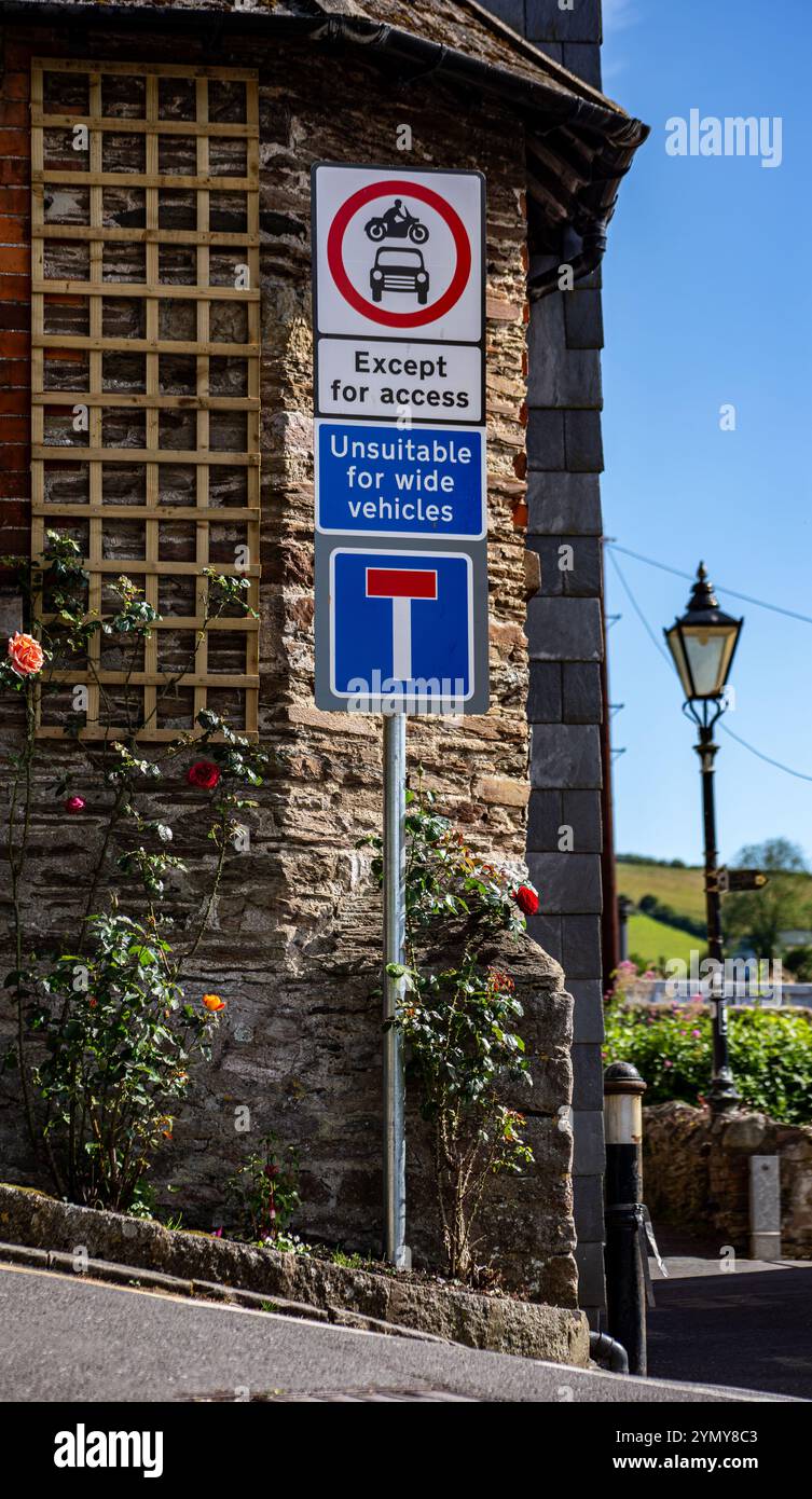 Cartello segnaletico in un pittoresco villaggio che mostra restrizioni stradali e una vista panoramica con lampione e fiori in fiore lungo un muro di pietra Kingswear Dartmouth Foto Stock