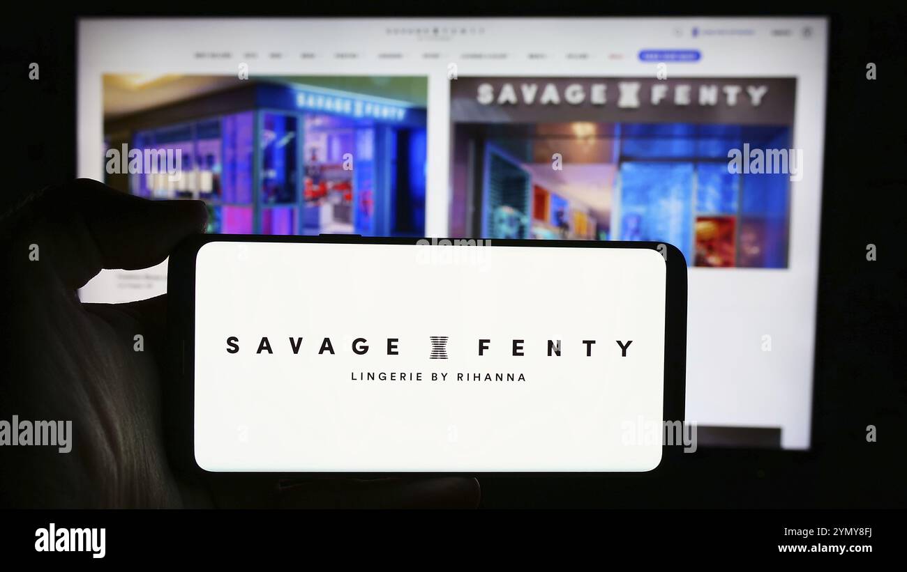 Stoccarda, Germania, 05-15-2024: Persona che tiene il cellulare con il logo della società di moda statunitense Savage X Fenty davanti alla pagina web aziendale. Concentrati sul telefono d Foto Stock