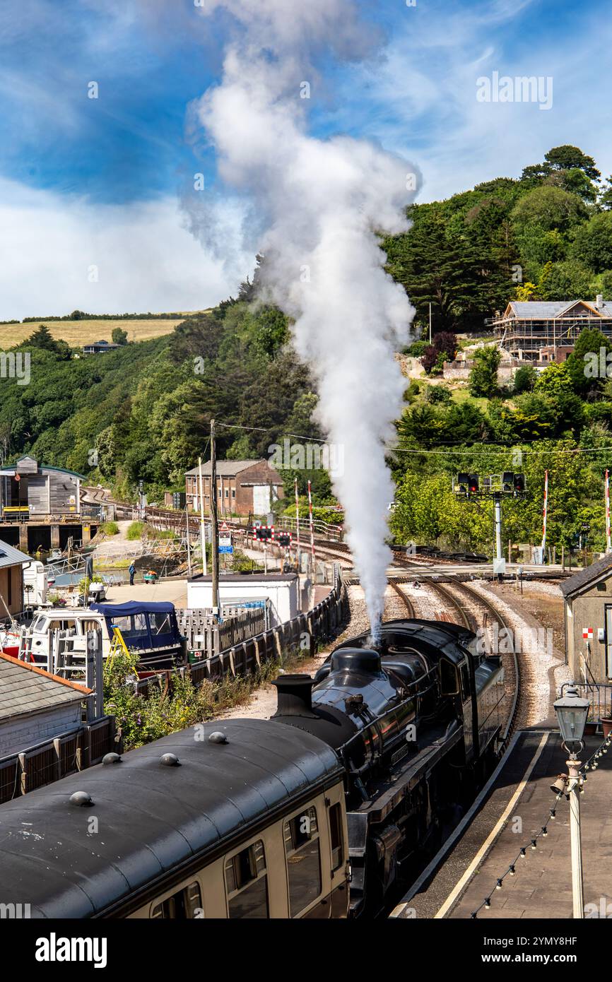Treno a vapore d'epoca con fumo che arriva alla stazione di Dartmouth in una giornata di sole con vedute panoramiche Foto Stock