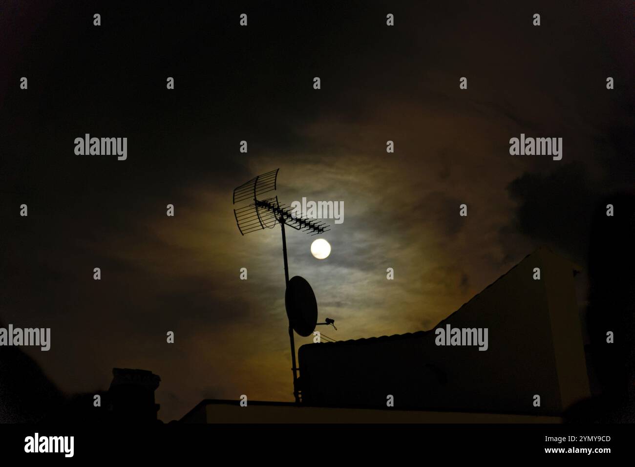 Luna piena in un cielo nuvoloso rosso che illumina un'antenna televisiva sul tetto Foto Stock