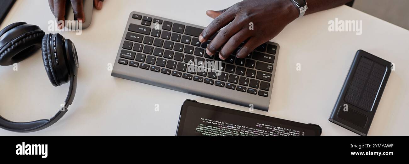 Primo piano delle mani digitando il codice sulla tastiera wireless durante il multitasking con i gadget su un'area di lavoro pulita senza disordine visibile. Foto Stock