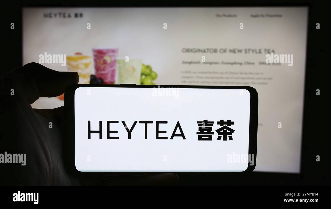 Stoccarda, Germania, 05-17-2024: Persona che tiene il cellulare con il logo della catena cinese di bevande Hey Tea (HeyTea) di fronte alla pagina web aziendale. Concentrati Foto Stock