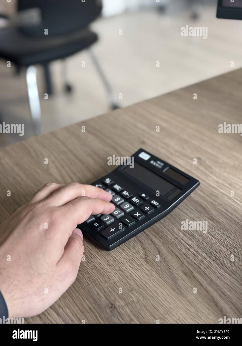 Una mano che preme i pulsanti su una calcolatrice nera su una scrivania in legno in un ufficio Foto Stock