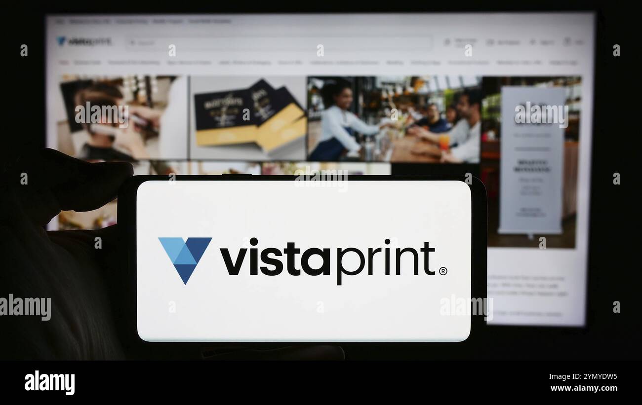 Stoccarda, Germania, 04-12-2024: Persona che detiene un cellulare con il logo della società di personalizzazione di massa Vistaprint (Vista) di fronte alla pagina web aziendale. Focu Foto Stock