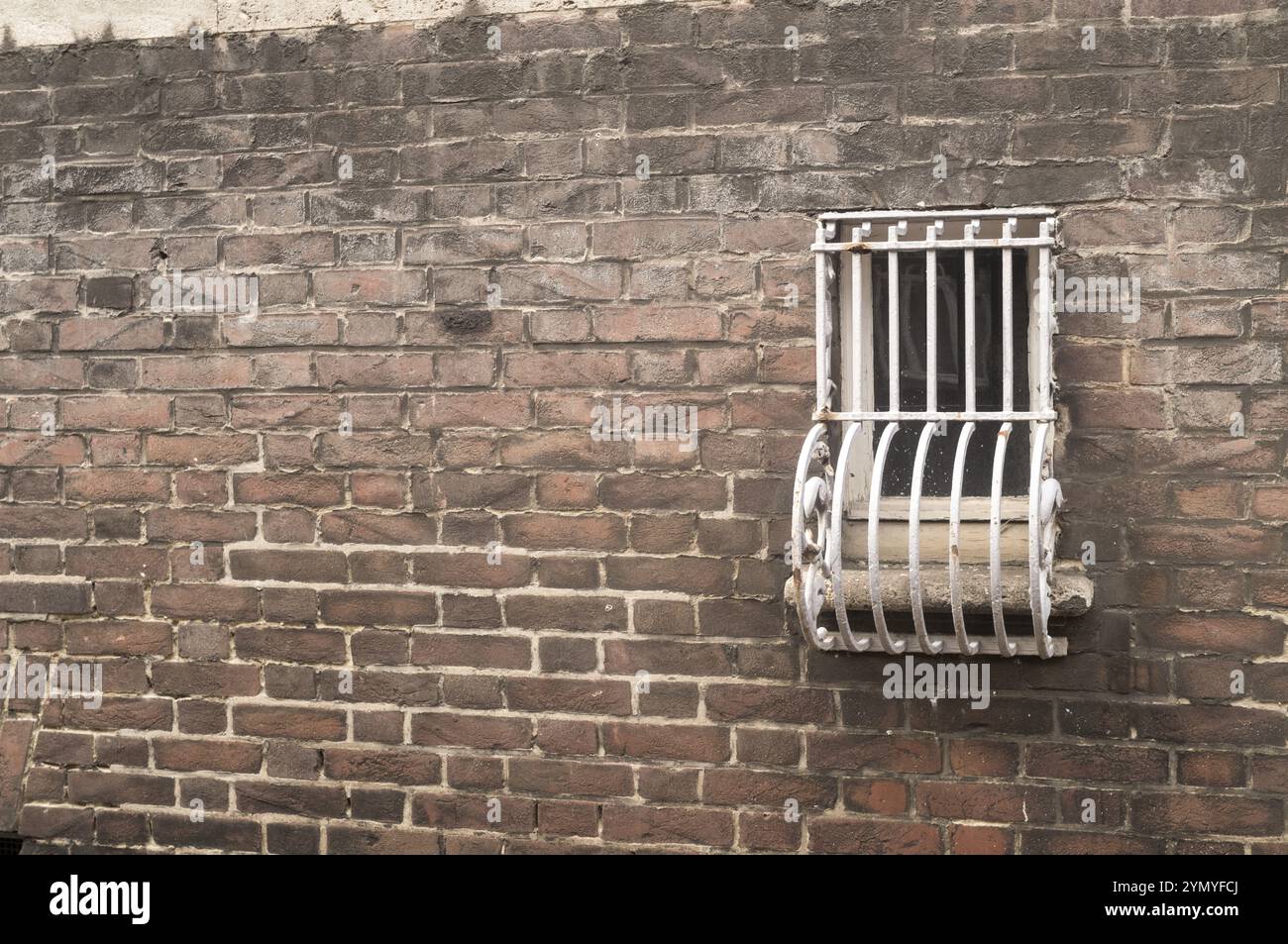 Piccola finestra sbarrata su un muro di mattoni Foto Stock