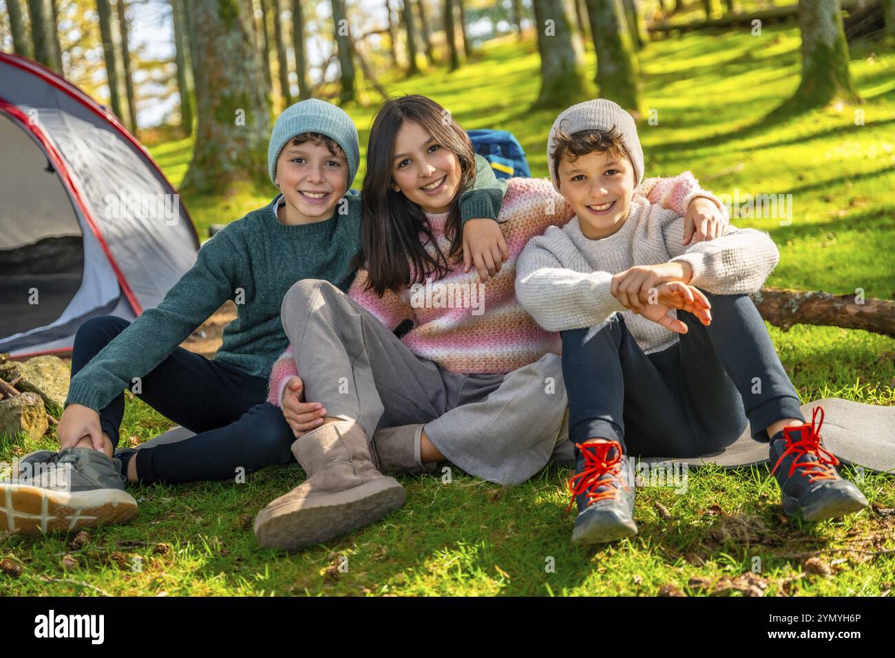 I problemi e la sorella seduti sull'erba nella foresta sorridono alla macchina fotografica mentre si divertono in campeggio Foto Stock
