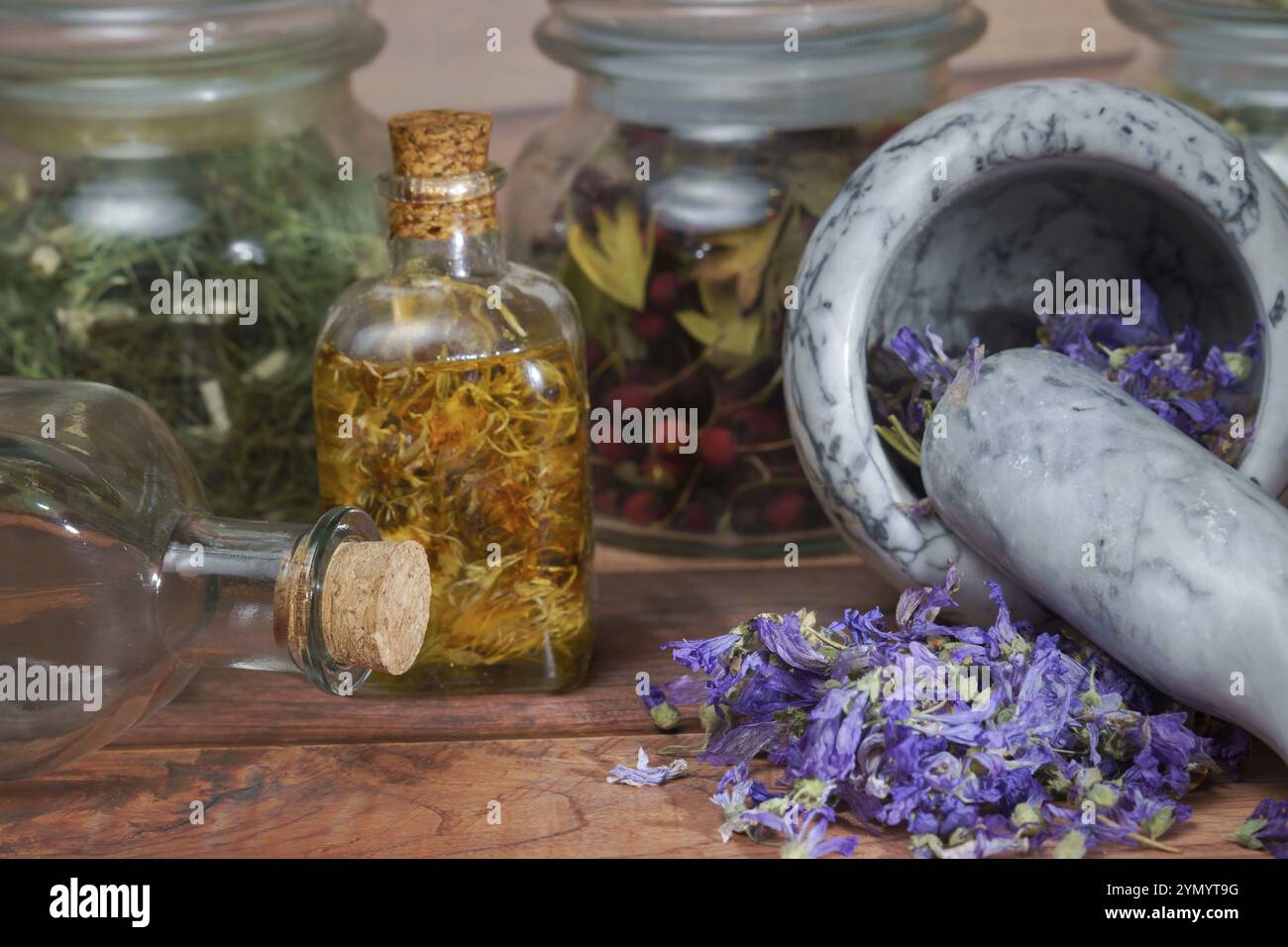 Schiacciamento di piante medicinali in mortaio e pestello con diverse preparazioni omeopatiche sullo sfondo Foto Stock