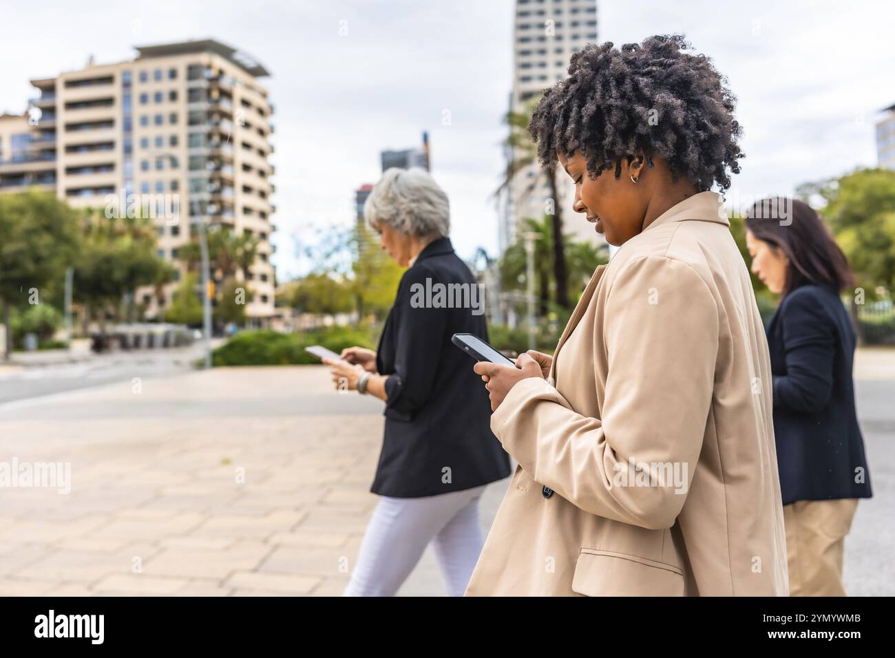 Vista laterale di uomini d'affari multietnici inglobati nei loro telefoni cellulari che camminano per la città Foto Stock