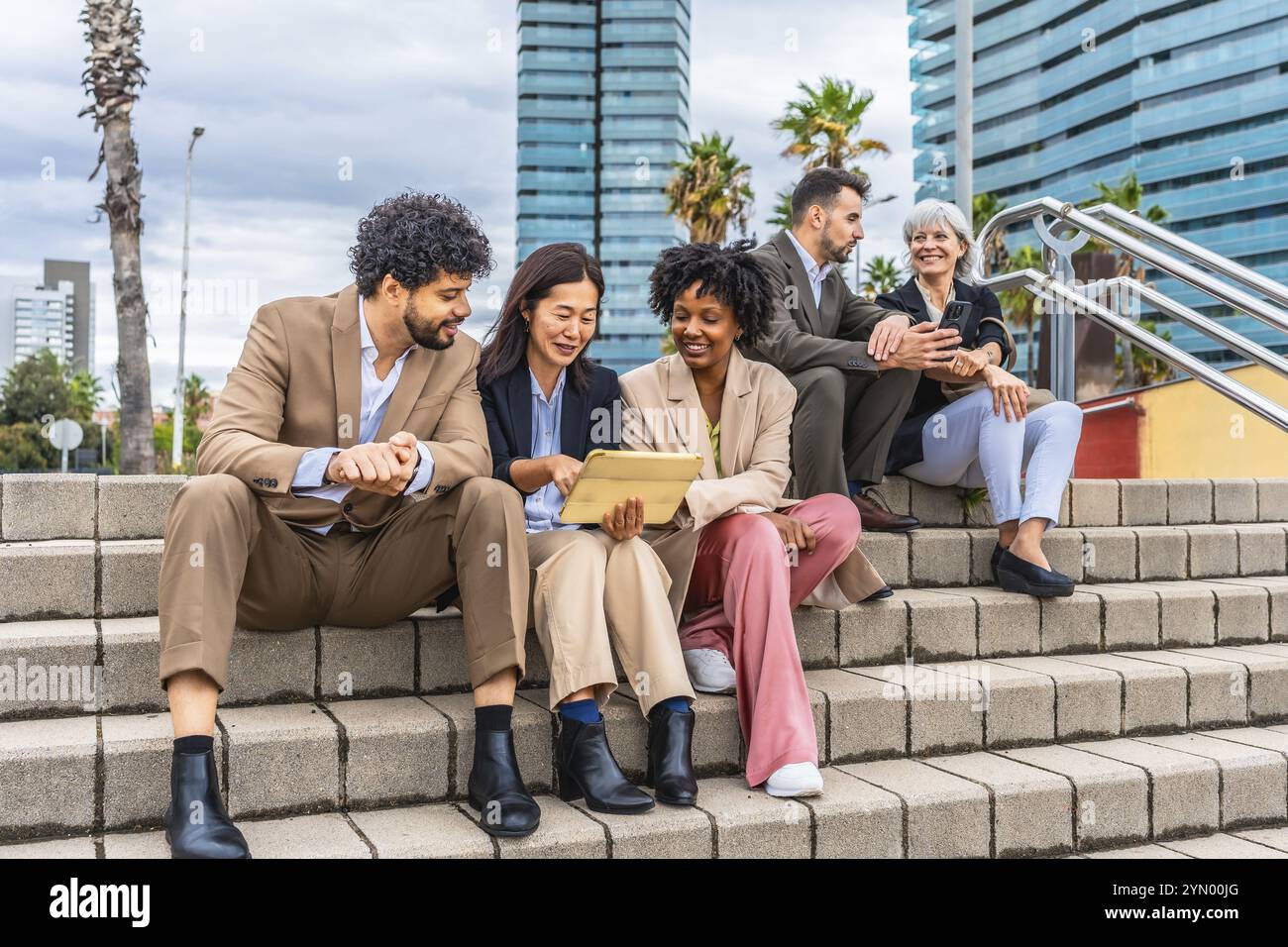 Gruppo multietnico e diversificato di uomini d'affari seduti su scale all'aperto che lavorano utilizzando un tablet digitale Foto Stock