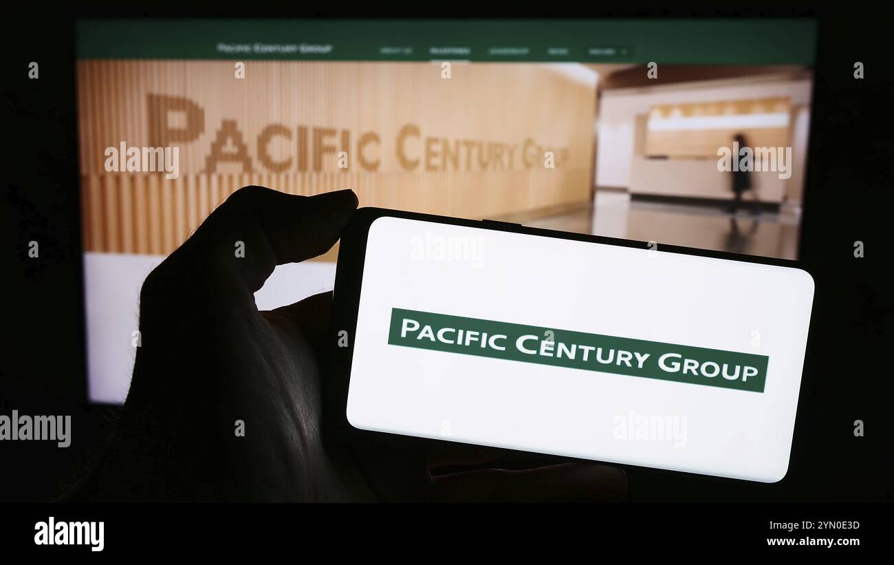 Stoccarda, Germania, 03-07-2024: Persona che detiene un telefono cellulare con il logo della società di investimento Pacific Century Group (PCG) di fronte alla pagina web aziendale. Foto Stock