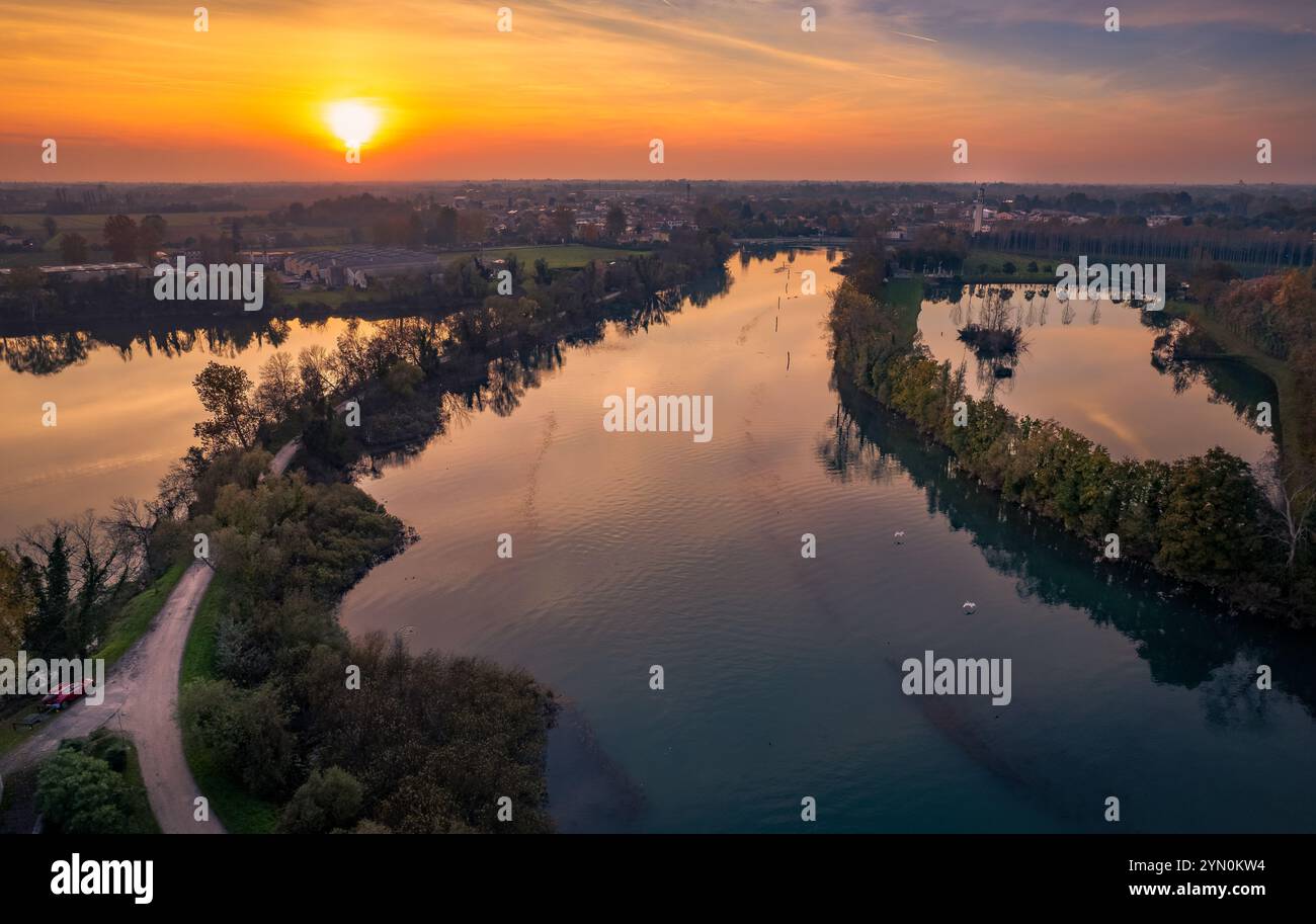 Un vivace tramonto proietta sfumature dorate sul fiume Sile, che si riflettono sulle sue acque calme. Vegetazione lussureggiante e sentieri tortuosi fiancheggiano le rive del fiume. Foto Stock