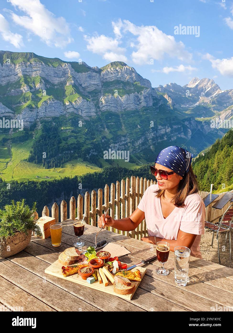 Una donna gode di un delizioso pasto su una terrazza che si affaccia sulle maestose montagne, circondata da una vegetazione vibrante. alpi svizzere, Ebenalp in Svizzera, Appenzell Foto Stock