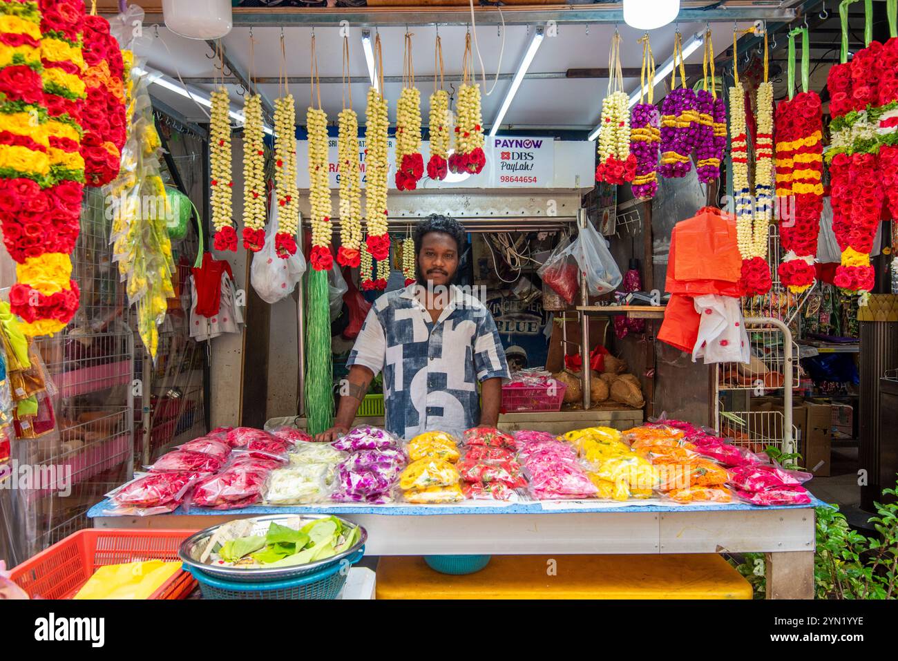 Un uomo in una stalla a Campbell Lane a Little India, Singapore, che vende fiori pressati e ghirlande di fiori colorati Foto Stock