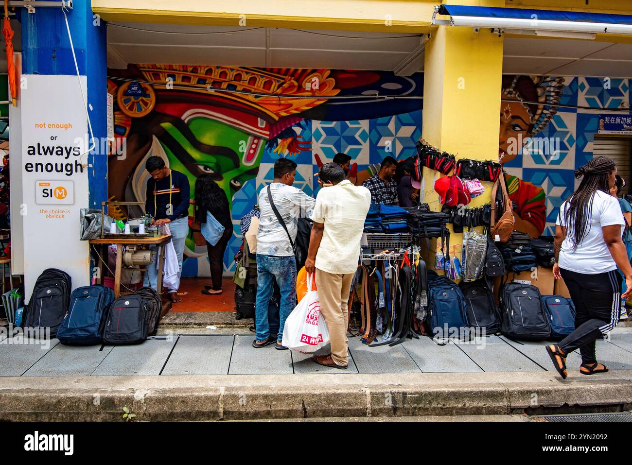 I pittoreschi murales indiani fanno da sfondo a una stalla che vende borse da viaggio e un sarto di modifiche a Campbell Lane, Little India a Singapore Foto Stock