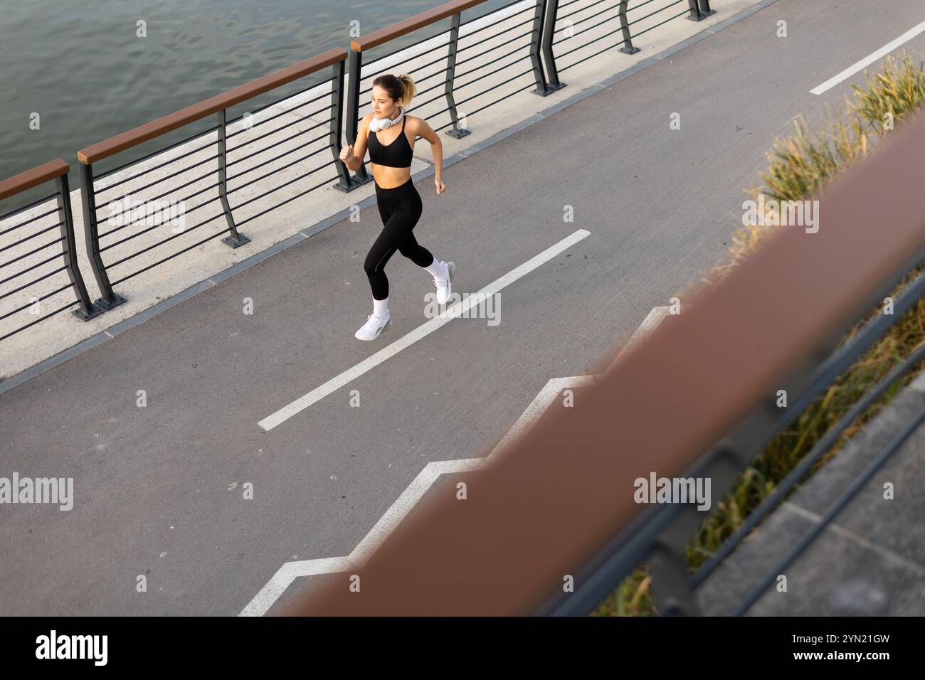 Una persona in abbigliamento attivo sta facendo jogging su un percorso ben tenuto accanto all'acqua serena, catturando l'essenza di un'energica routine mattutina in città. Foto Stock