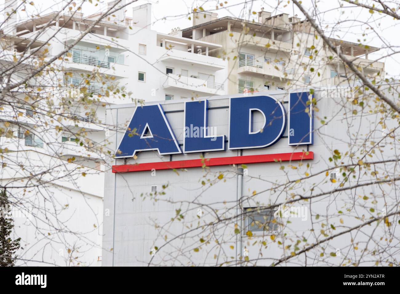 Insegna del supermercato Aldi esposta sull'esterno dell'edificio con rami di alberi in primo piano Foto Stock