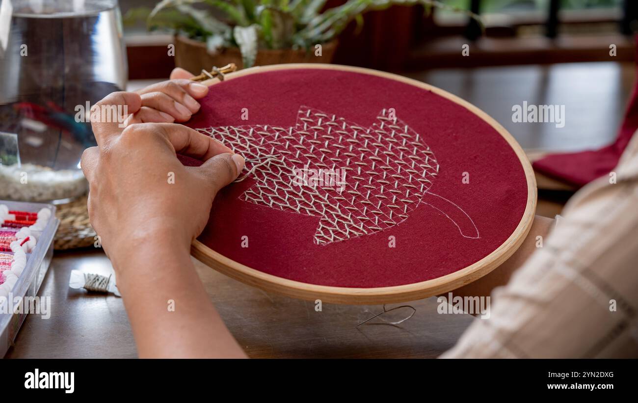 Arte del ricamo a mano: Come cucire un motivo a foglia su un tessuto rosso Foto Stock