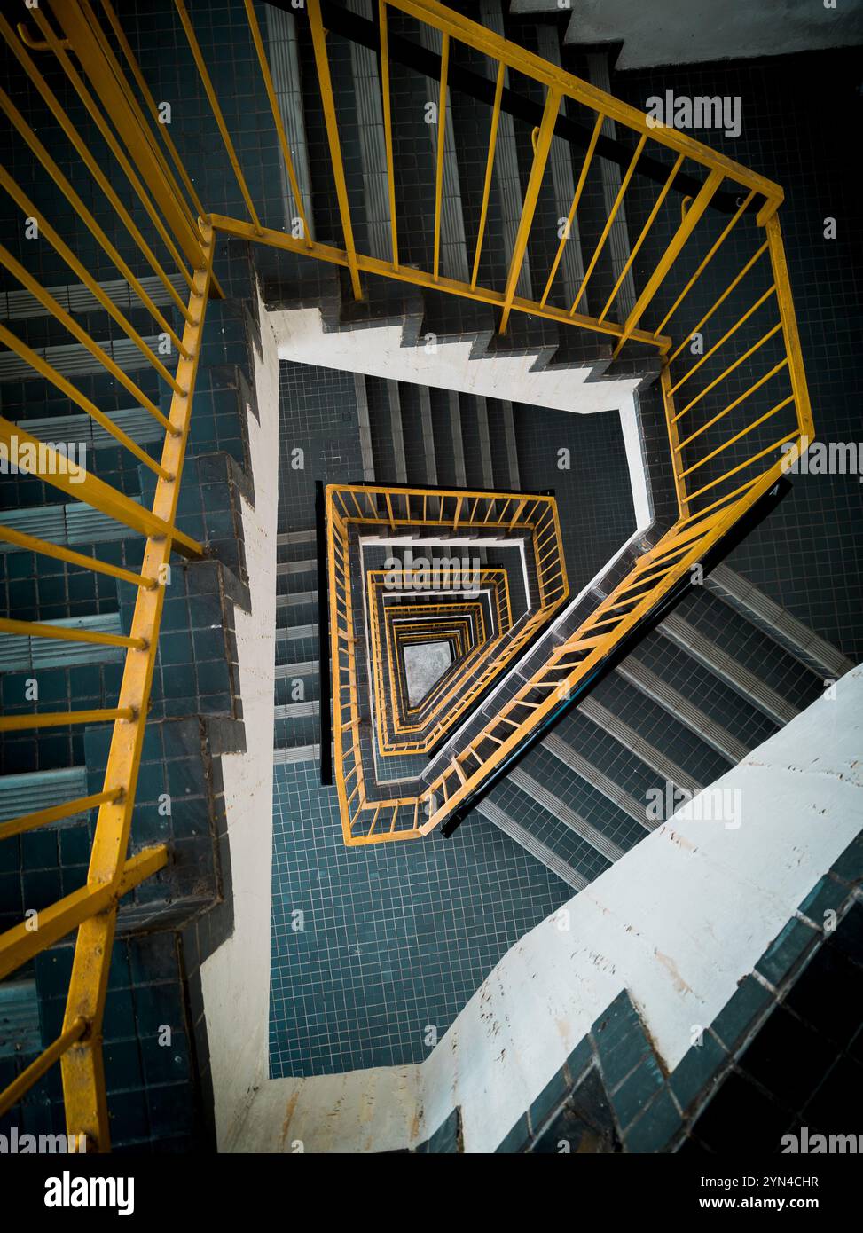 "Prospettiva astratta della scala a spirale con rotaie gialle e motivi geometrici delle piastrelle nel design degli interni urbani" Foto Stock