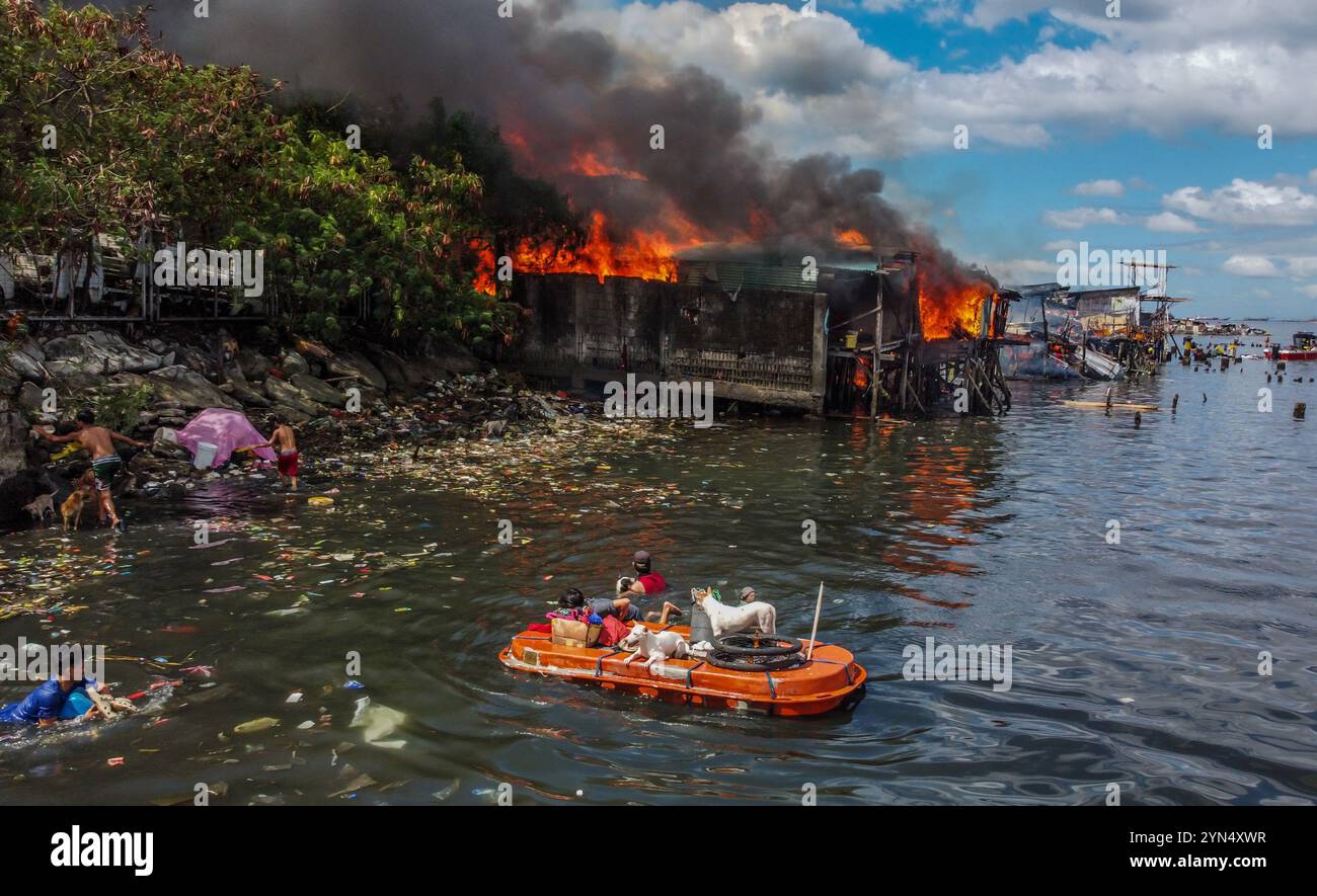 Manila. 24 novembre 2024. I residenti usano una barca improvvisata per evacuare con i loro cani da compagnia e i loro effetti personali come un incendio inghiottisce un'area di slum a Manila, nelle Filippine, il 24 novembre 2024. Crediti: Rouelle Umali/Xinhua/Alamy Live News Foto Stock