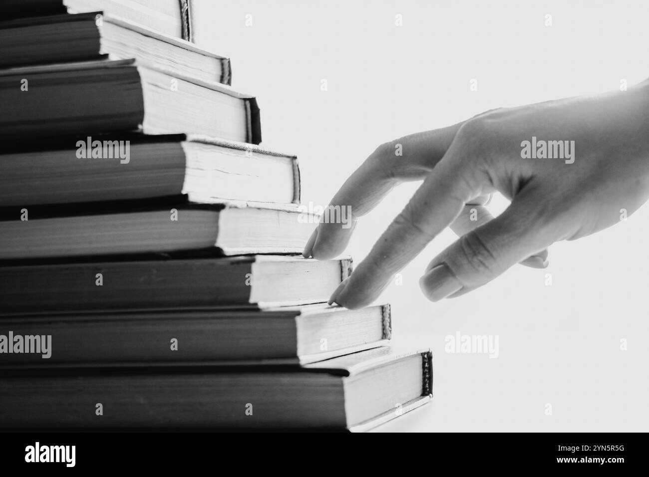 La mano di una ragazza si arrampica su gradini fatti di libri, percorso verso il successo, superare le difficoltà, scalare gradini Foto Stock