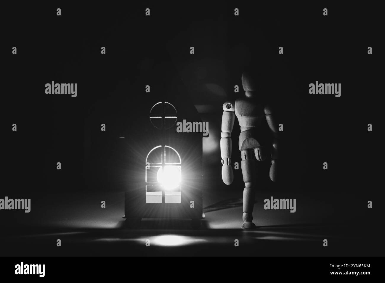 Una bambola di legno a una gamba si trova vicino a una casa con raggi di luce da una finestra al buio, una bambola senza gambe vicino a una casa Foto Stock