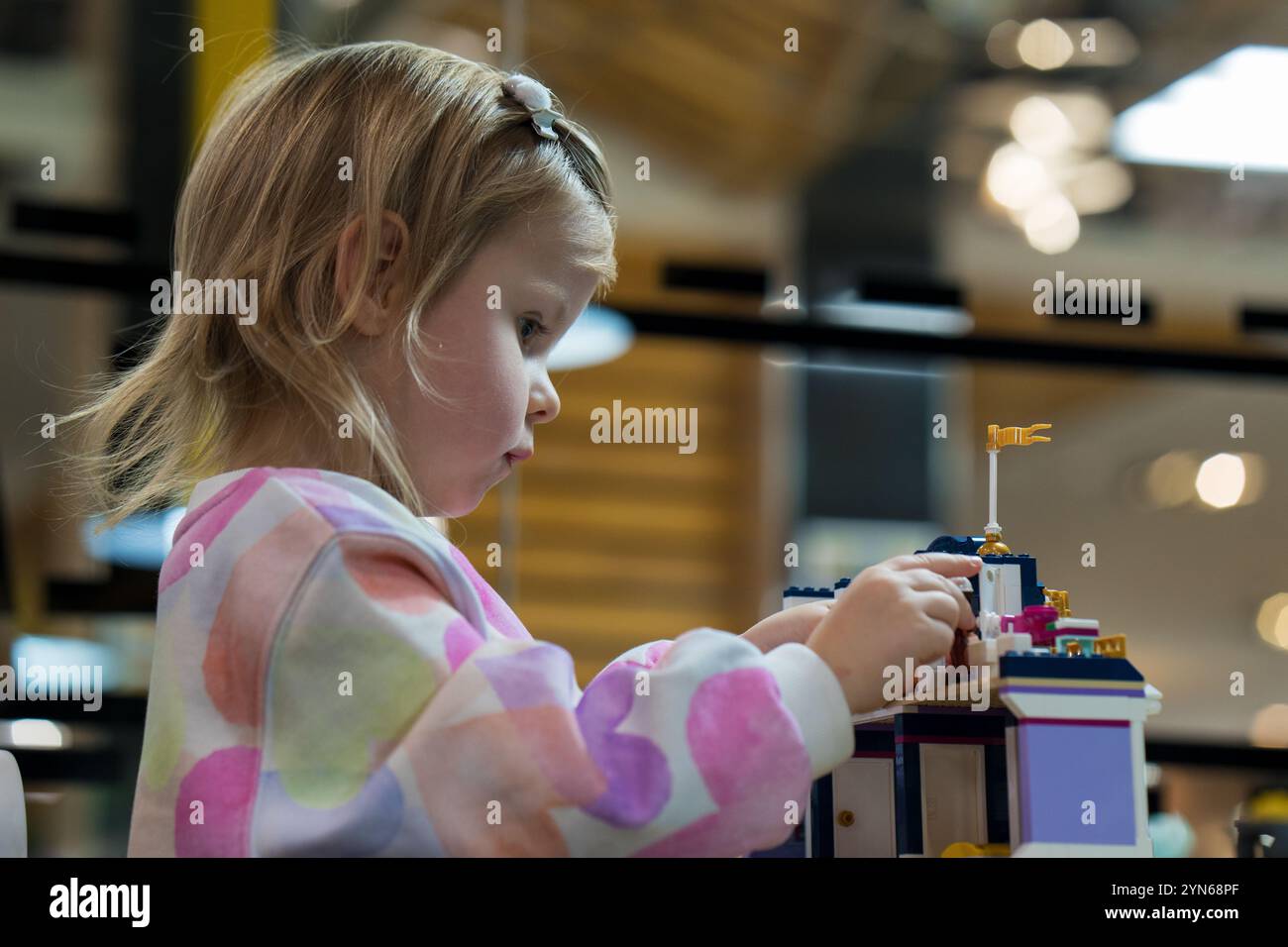 Sala giochi per bambini. Una bambina carina gioca con le parti colorate in plastica del costruttore, crea edifici, attrezzature, trasporti. Foto Stock