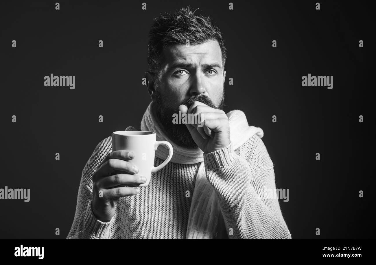 Uomo barbuto con mal di gola, tosse nel pugno e beveva una bevanda curativa dalla tazza. Uomo malvagio che tossisce. Uomo malato in maglione e sciarpa con Foto Stock